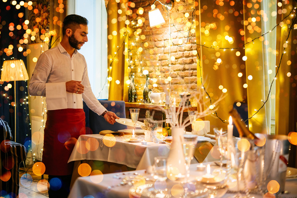 A waiter puts a plate on a festively decorated table. 
