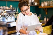 Une employée de restaurant travaille sur une table avec un téléphone sous l'oreille. 