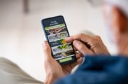 An over-the-shoulder view of someone holding a phone looking at a food-ordering app. 