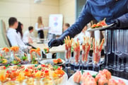 A caterer adds the final touches to a table of food while a business meeting goes on in the background. 