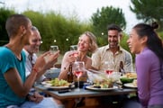 Smiling people share a meal around a restaurant patio table.