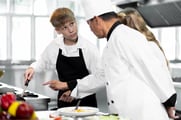A chef works with two trainees in a restaurant kitchen.