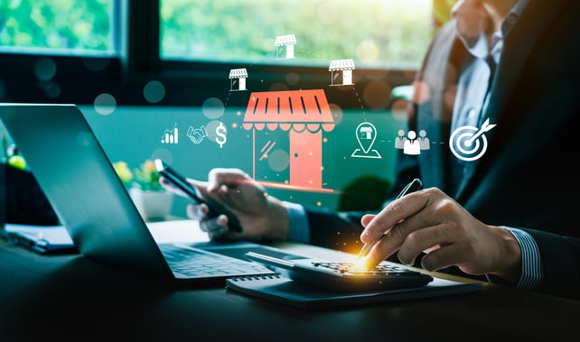 Une personne est assise devant un ordinateur portable, un téléphone dans une main et une calculatrice dans l'autre ; des icônes flottantes indiquent qu'elle consulte des données marketing. 