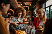 A server puts a juicy hamburger down on a table with smiling people seated around it.