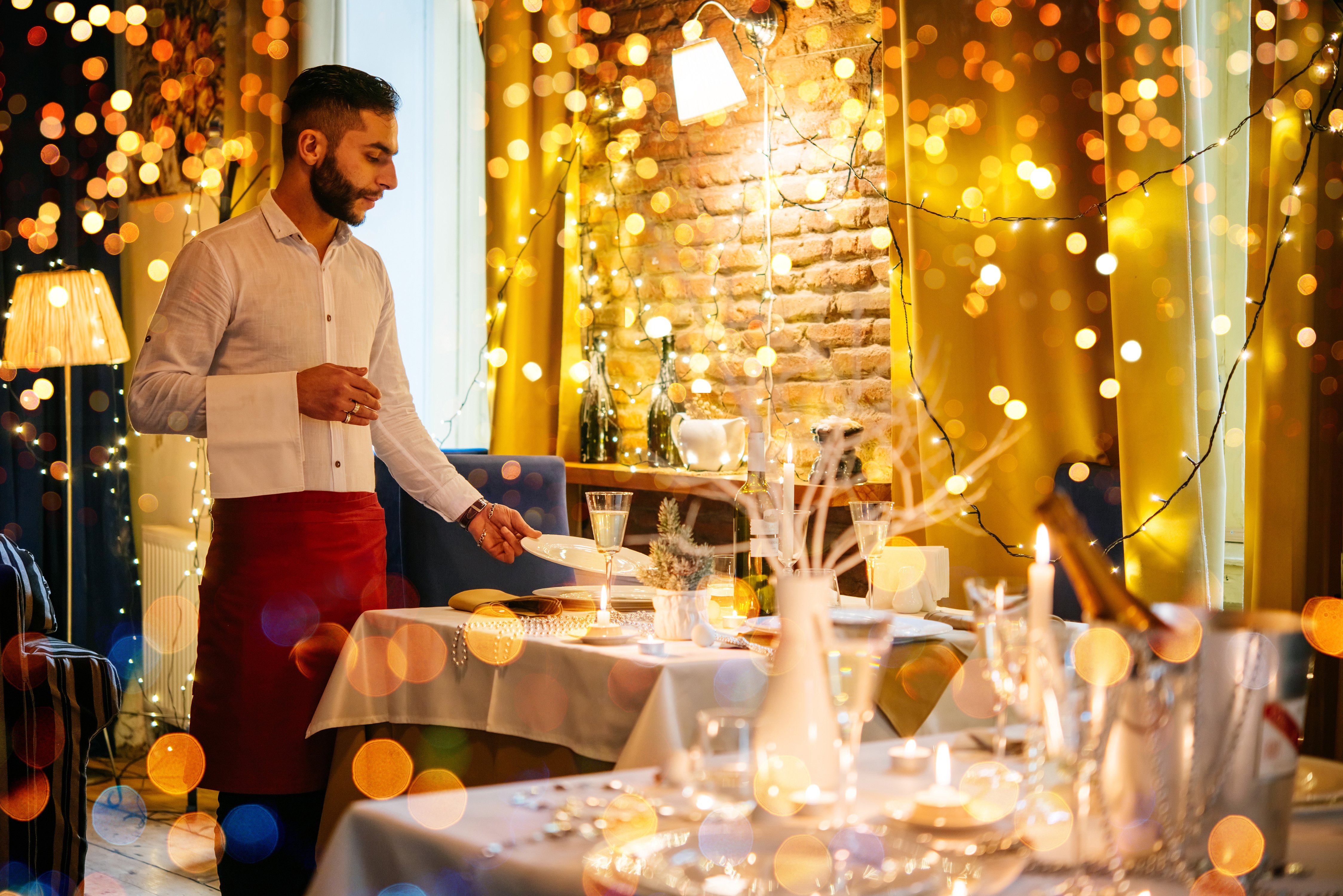 A waiter puts a plate on a festively decorated table.