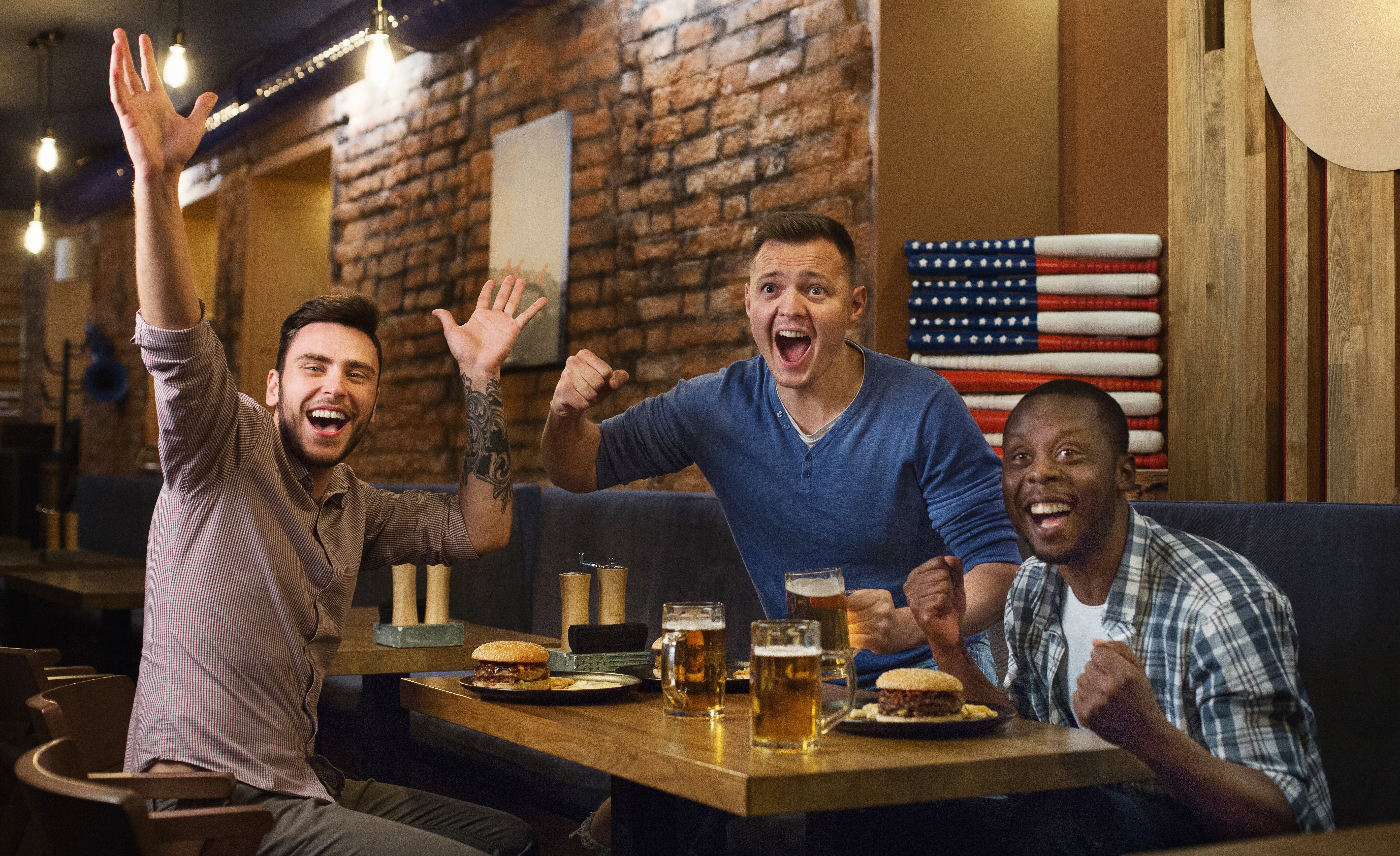 Three men enjoy burgers and beer while cheering on their team.