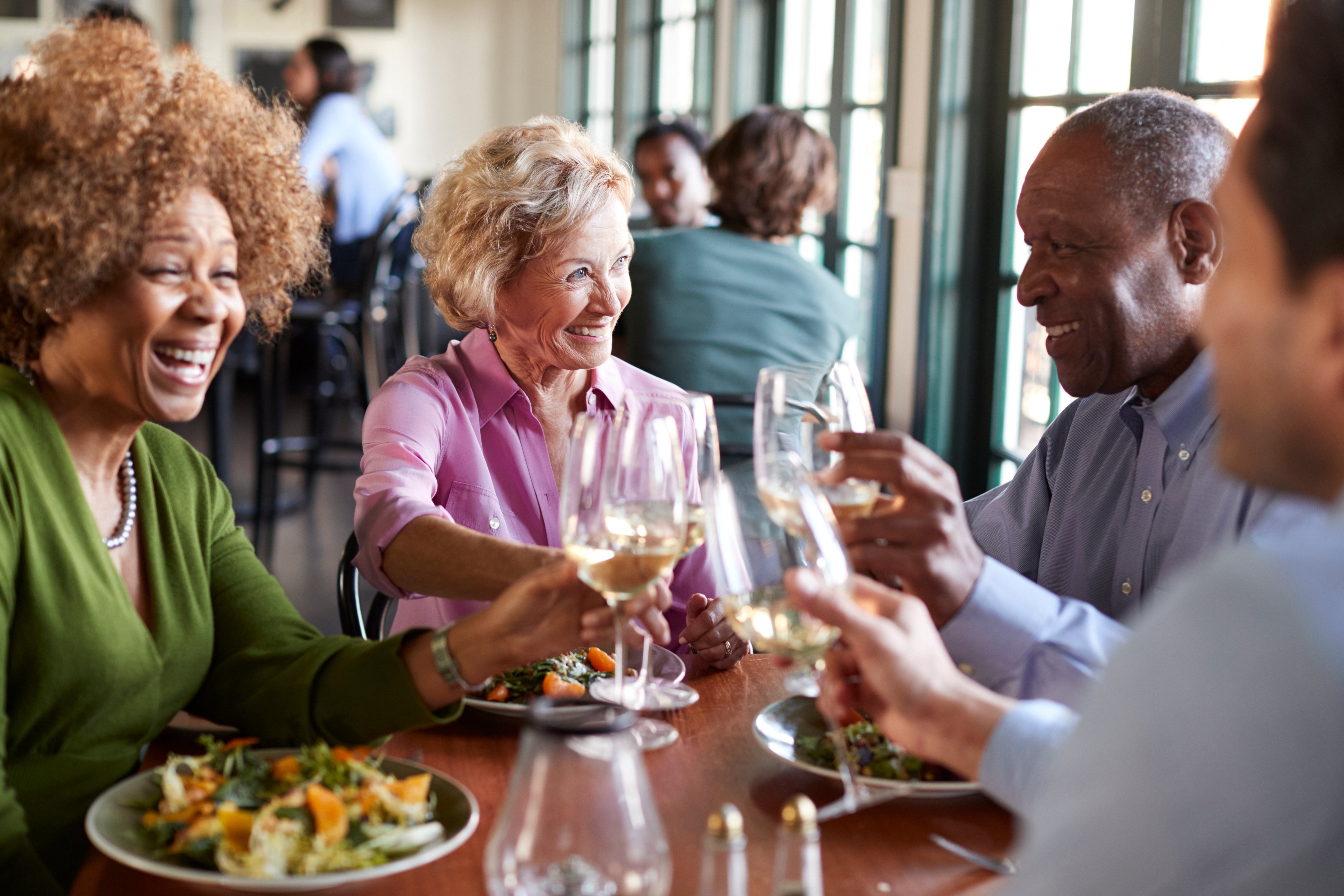 Four smiling seniors toast each other with wineglasses around a restaurant table.